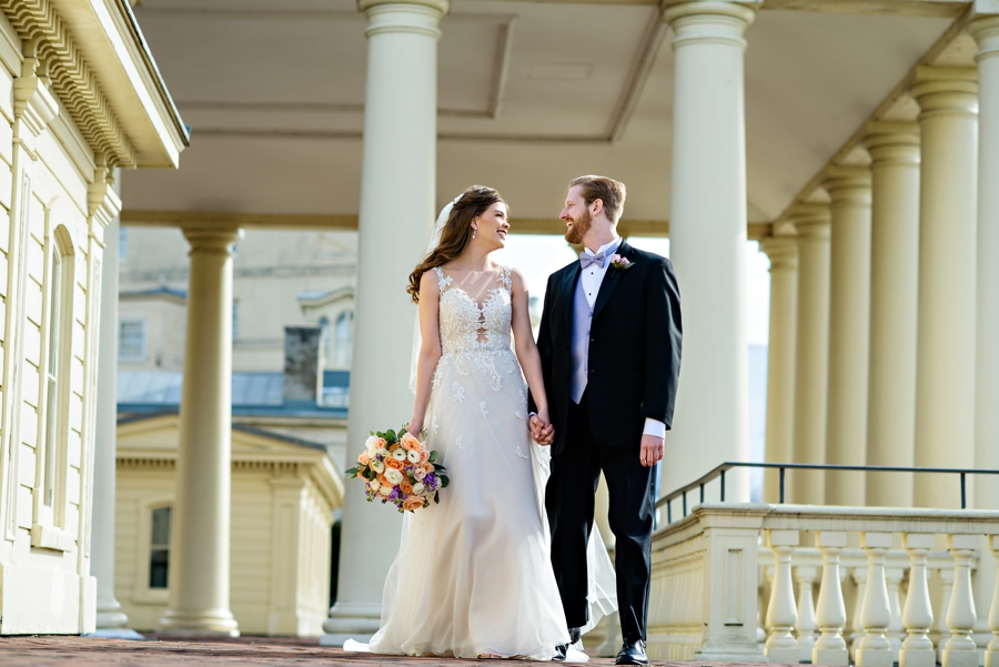 A bride and groom walk along the Schuylkill river under the columned walkways at their Water Works Wedding in Philadelphia.